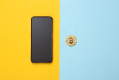 Bitcoin and smartphone on a blue-yellow background. Cryptocurrencyの写真素材