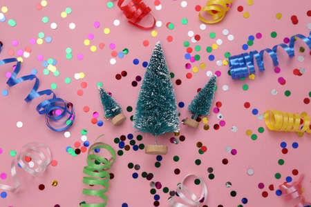 Christmas mini trees and colored serpentine with confetti on a pink background. christmas background