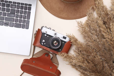 autumn creative composition. Beige reeds branches, camera, hat and laptop on beige background. travel concept. flat layの写真素材