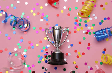 Winner cup and colored serpentine with confetti on a pink background. Winning the competition, awarding the winnerの写真素材