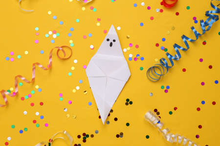 Origami Halloween ghost with colored streamer with confetti on yellow background. Halloween...