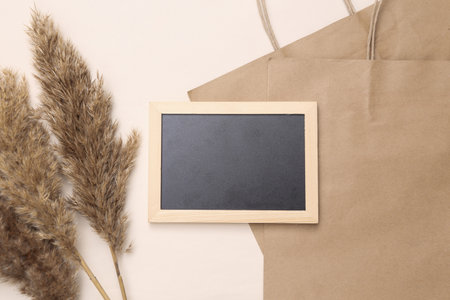 Natural, eco composition with paper shopping bags, reed branches, empty chalk board on a light beige background. Copy space. Flat lay, top viewの写真素材