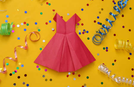 Origami red dress with Colored streamer and confetti on yellow background. Holiday, birhday...