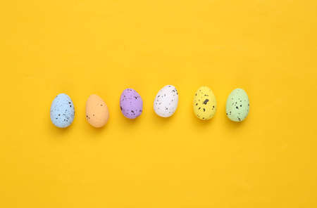 Colored quail eggs on yellow background. Easter composition. top view