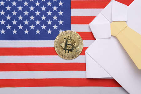 Cryptocurrency, economy and trading concept. Golden bitcoin and origami shirt with tie on USA flag backgroundの写真素材