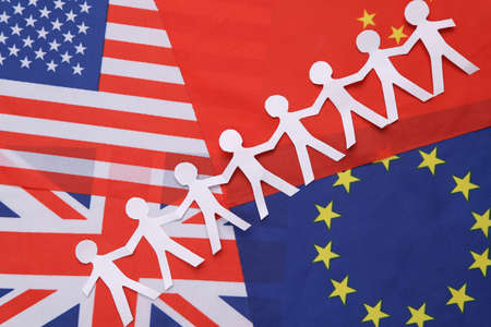 Chain of paper-cut people against the background of the many flags. unity concept. Together we are strongerの写真素材