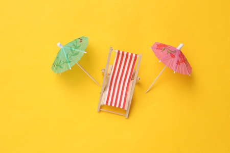 Mini beach deck chair with umbrella on a yellow background. Beach vacation, summer time, sunbathing conceptの写真素材