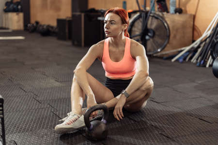 Tired fit woman resting after intense workout with kettlebell in the gymの写真素材
