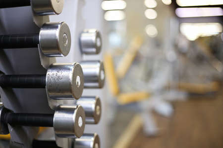 Rack with metal dumbbells on blurred gym background