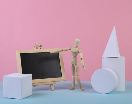 Empty chalk board with wooden puppet and geometric shapes on blue pink pastel background. Abstract background, concept art, minimalism. school composition. copy spaceの写真素材