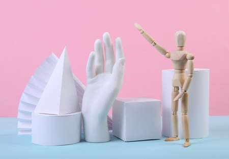 Geometric figures, wooden puppet and hand on a blue-pink pastel background. Composition of different geometric objects. concept art. Abstract background, minimalismの写真素材