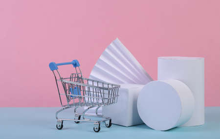 Shopping trolley and geometric shapes on blue pink pastel background. sale, product presentation. Abstract background, concept art, minimalism. geometric compositionの写真素材