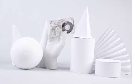 The mannequin's hand holds audio cassette and geometric shapes on white background. fashion...