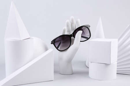 Stand hand holding sunglasses and geometric shapes on white background. concept art. minimalism
