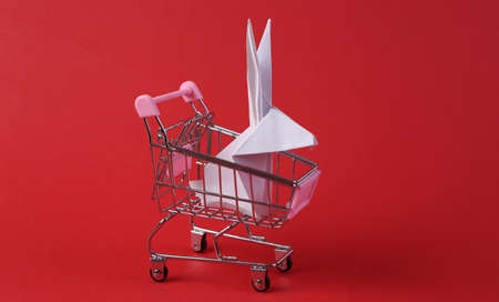 Mini shopping cart with origami easter bunny on red backgroundの写真素材