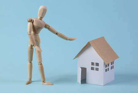home sale concept. Puppet realtor points to a house figurine on a blue backgroundの写真素材
