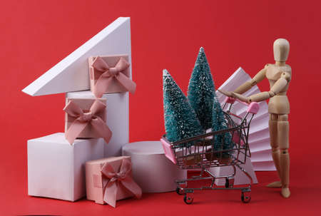 Christmas still life. Geometric shapes, shopping trolley, puppet, mini Christmas trees and gift boxes on red background. Concept art, minimalismの写真素材
