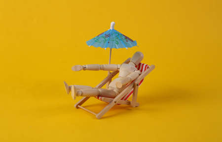 Deck chair with umbrella, wooden puppet rest on yellow background. beach rest conceptの写真素材