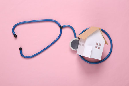 Mini paper home figurine and stethoscope on pink background. Home medicine, family doctorの写真素材