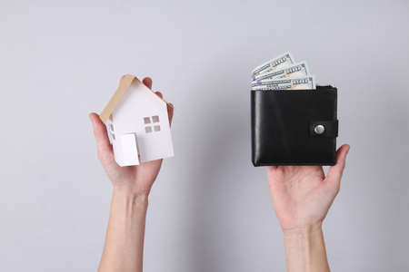 Home buying concept. Hands hold mini house and purse on gray backgroundの写真素材
