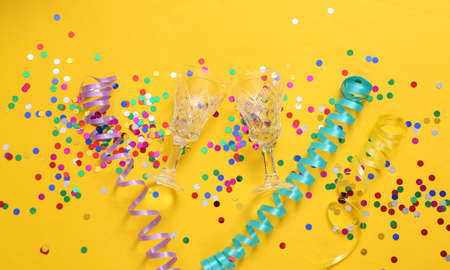 Glasses and confetti with streamer on yellow background