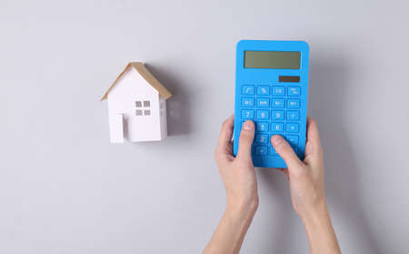 Hand uses calculator on a gray background with a house. Calculating the cost of housing rentの写真素材