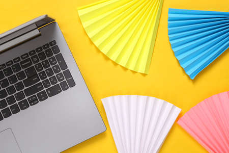 Laptop and paper fans on yellow background