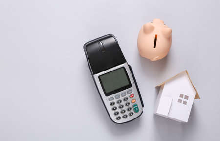 Home buying concept. Mini house, payment terminal and piggy bank on gray background. top view