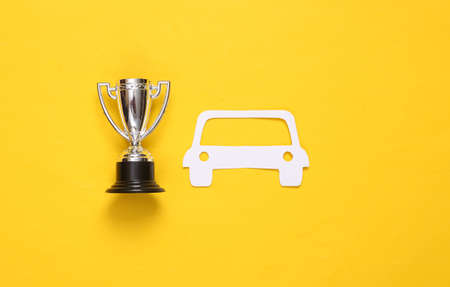 Paper cut car and winner cup on yellow background. auto racing