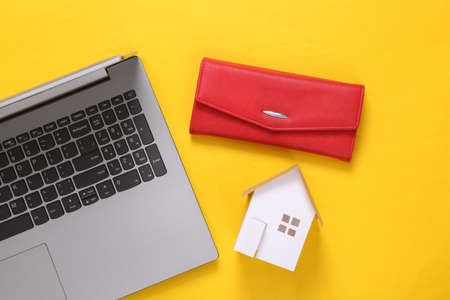 Home buying concept. Laptop, Mini house and purse on yellow background