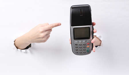 Female hands holding payment terminal through torn hole white paper. concept art