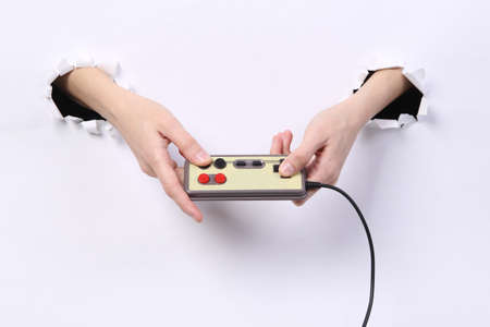 Female hands holding retro gamepad through torn hole white paper. concept art