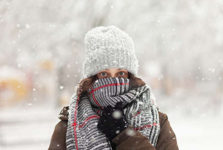 Portrait of a woman wrapped in a scarf and in a warm hat in winter snowy weatherの写真素材
