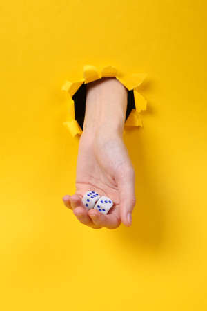 Female hand holds dice through torn hole yellow paper. Gambling addiction. concept art.の写真素材
