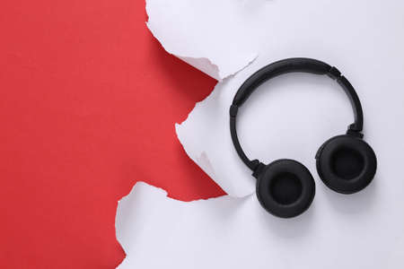Stereo headphones and torn paper sheet on red background. top view.