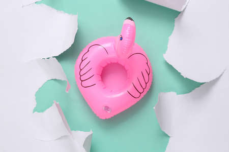 Inflatable flamingo on blue background with white torn paper. Beach Rest Concept. minimalism. top...