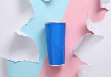 Cardboard drink cup with straw on blue-pink background with torn paper. concept art. Pastel color trend. top viewの写真素材