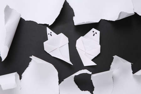 Origami ghosts and white torn paper sheet on black background. helloween concept. minimalism. top viewの写真素材