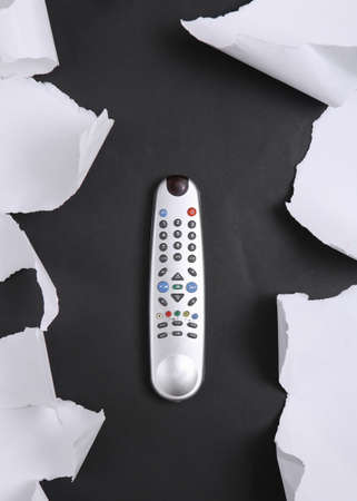 Tv remote on black background with white torn paper. concept art. minimalism. top view