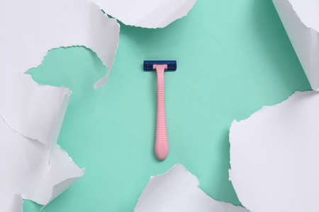 Razor epilator on blue background with white torn paper. beauty concept. minimalism. top view