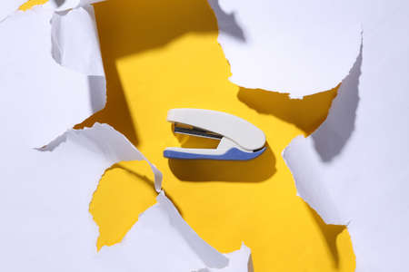 Stapler on yellow background with white torn paper. minimalism. trend shadow. top view