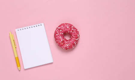 Weight loss plan, or recipe for cooking. Notepad with pen and donut on a pink background. top viewの写真素材