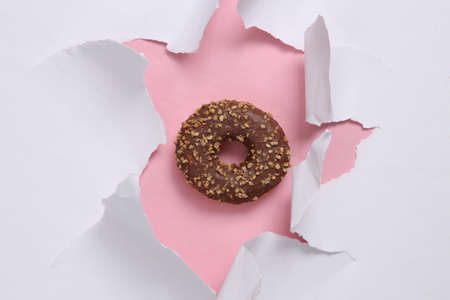 Delicious sweet donut through the torn hole of the paper. concept art. minimalismの写真素材