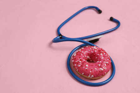health care. Stethoscope and high-calorie donut on a pink background. junk foodの写真素材