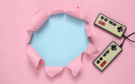 Torn hole and retro gamepads on blue-pink pastel background. concept art. Pastel color trend....