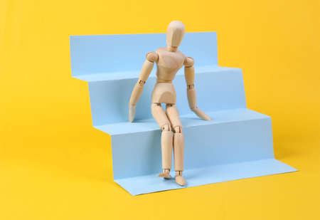 Wooden puppet on stairs podium, yellow background. Concept art, minimalismの写真素材