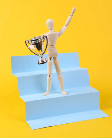 Puppet with the winner's cup on the stairs podium. yellow background