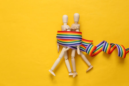 Lgbt relationships. Two puppets on yellow background with a rainbow ribbonの写真素材