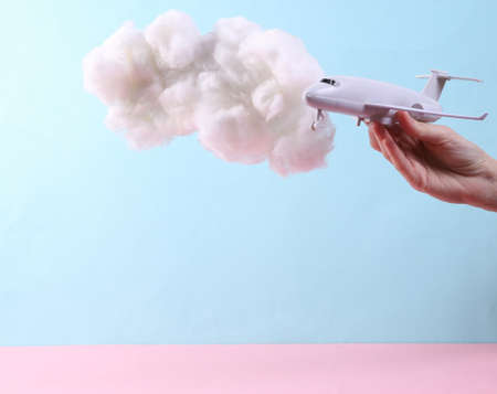 Hand holding Toy air plane with fluffy cloud on pastel blue background. creative ideas. Minimal...