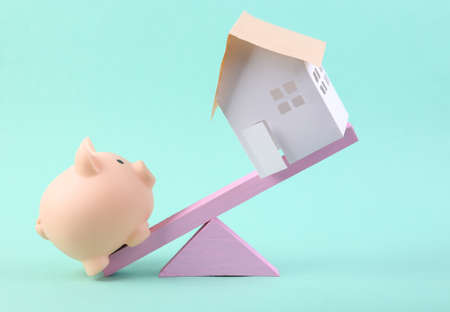 Balancing swing with piggy bank and house on a blue background. minimalism.の写真素材